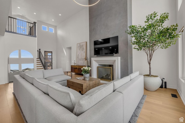 living area featuring stairs, wood finished floors, a glass covered fireplace, visible vents, and recessed lighting