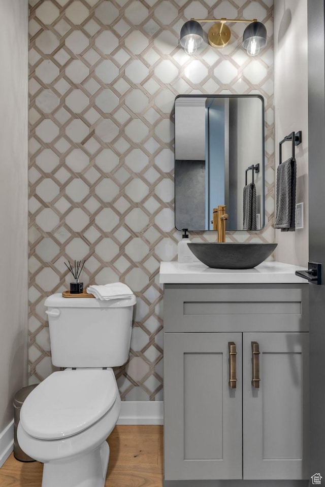 bathroom with toilet, vanity, wood finished floors, baseboards, and wallpapered walls