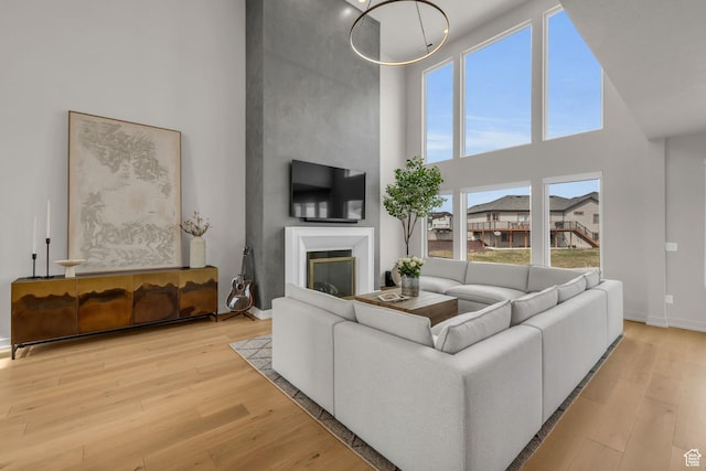 living area featuring baseboards, a towering ceiling, a glass covered fireplace, and light wood-type flooring