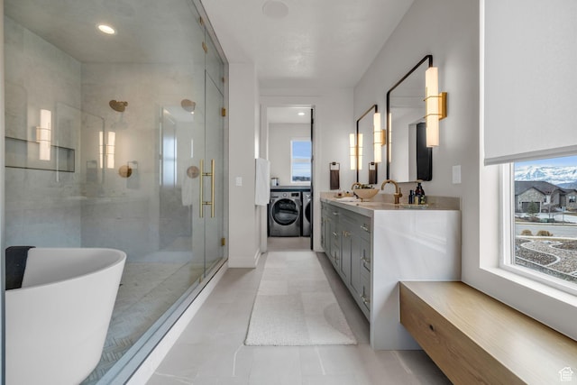bathroom featuring a shower stall, a sink, a freestanding bath, double vanity, and washing machine and dryer