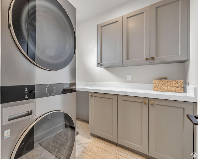 washroom with marble finish floor, cabinet space, and stacked washer / drying machine