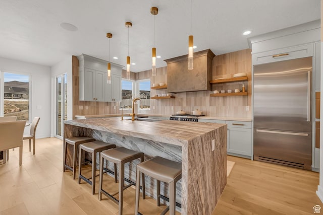 kitchen featuring a sink, open shelves, tasteful backsplash, built in refrigerator, and light wood-style floors