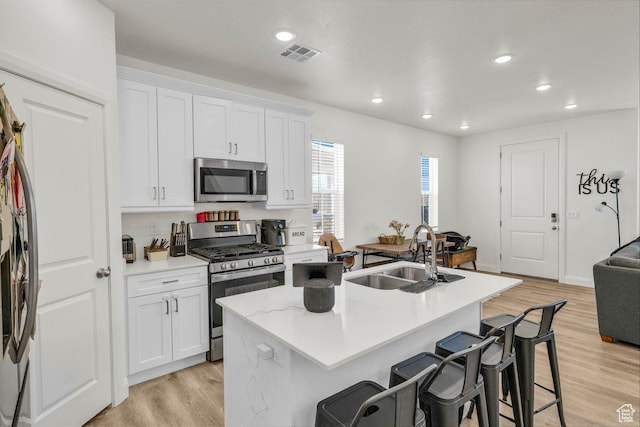 kitchen with a kitchen breakfast bar, stainless steel appliances, a sink, light wood finished floors, and visible vents
