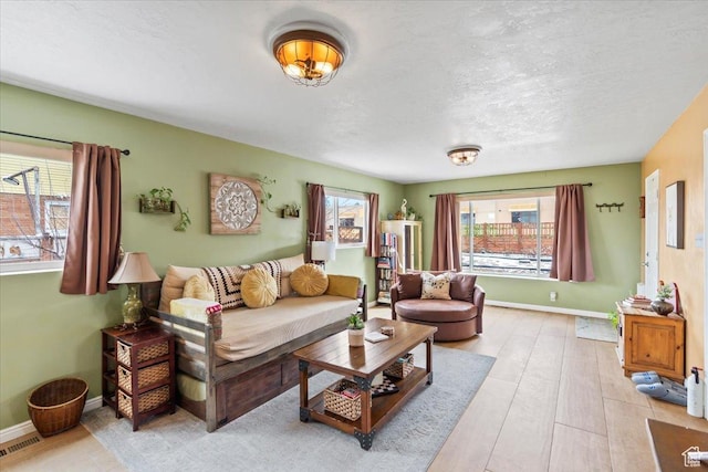 living area featuring baseboards, a textured ceiling, visible vents, and light wood-style floors