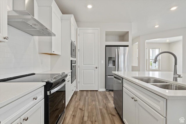 kitchen featuring light countertops, a sink, wall chimney range hood, white cabinets, and appliances with stainless steel finishes