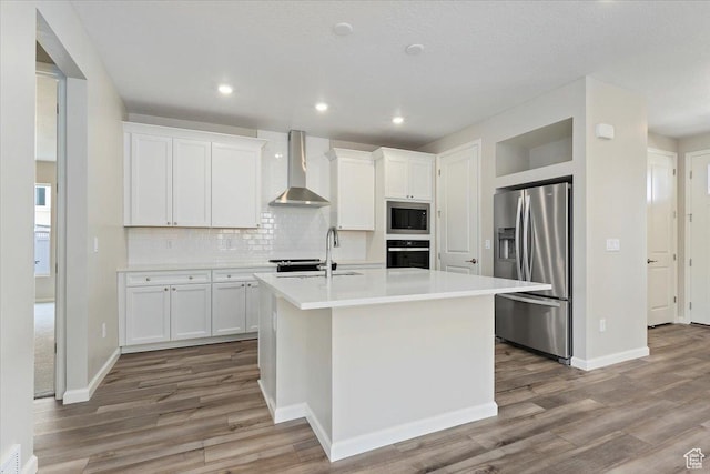kitchen with white cabinets, light countertops, appliances with stainless steel finishes, a sink, and wall chimney range hood