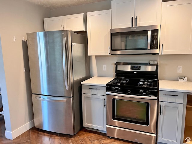 kitchen featuring baseboards, white cabinetry, parquet floors, and appliances with stainless steel finishes
