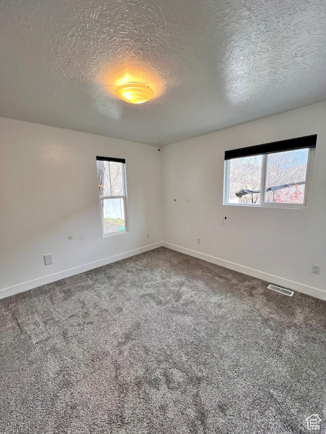 spare room featuring carpet floors, a textured ceiling, baseboards, and visible vents
