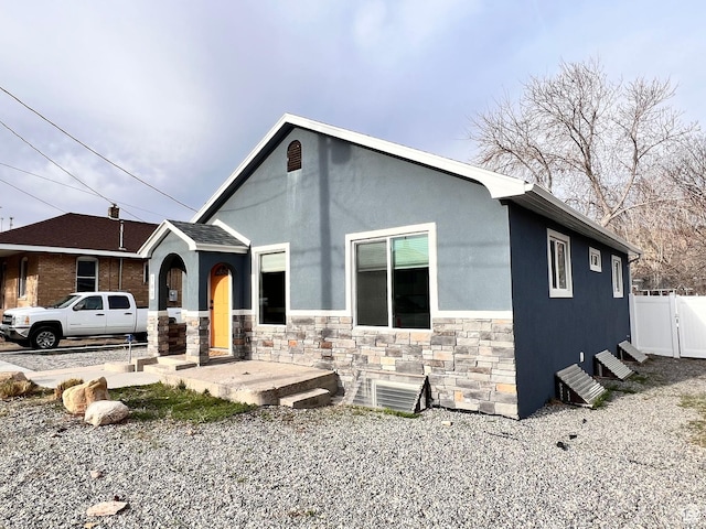 view of front of house featuring stucco siding, a gate, fence, and stone siding