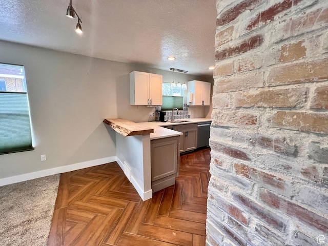 kitchen featuring a textured ceiling, light countertops, a peninsula, dishwasher, and baseboards