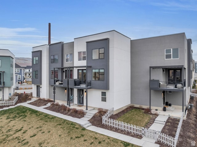 exterior space featuring a balcony, stucco siding, a front lawn, and fence private yard