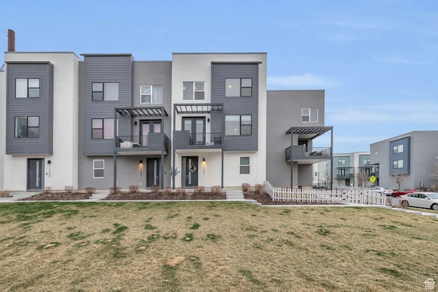 view of property with a balcony, a front yard, stucco siding, and fence