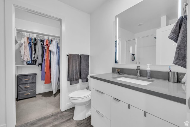 full bath featuring a shower, toilet, wood finished floors, vanity, and a spacious closet