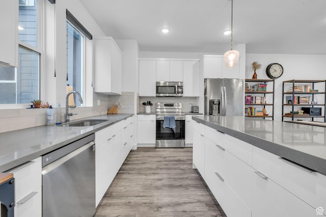 kitchen with modern cabinets, stainless steel appliances, white cabinetry, a sink, and backsplash