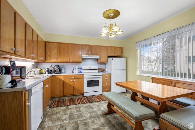 kitchen with a chandelier, white appliances, under cabinet range hood, a sink, and brown cabinetry