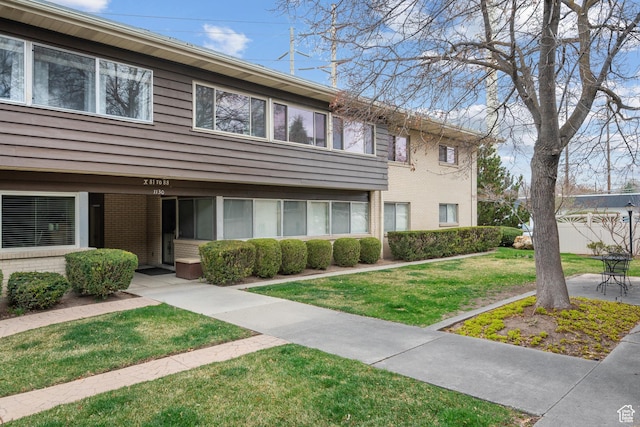 townhome / multi-family property featuring a patio area, brick siding, fence, and a front lawn