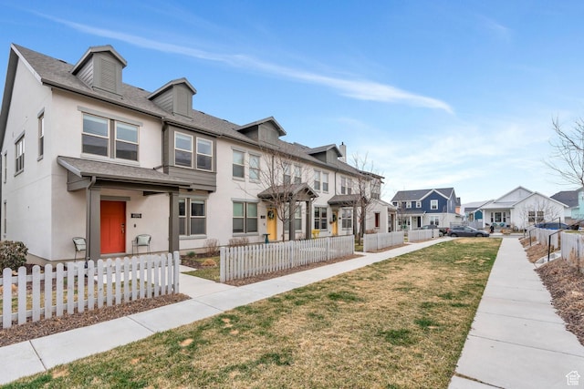 view of front of property featuring stucco siding, fence, a front lawn, a residential view, and a shingled roof