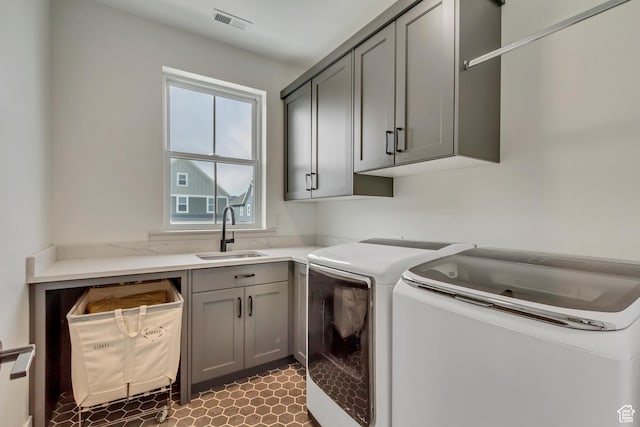 washroom featuring washing machine and clothes dryer, a sink, cabinet space, and visible vents