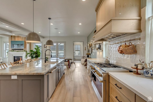 kitchen featuring decorative backsplash, custom exhaust hood, a sink, light wood-style floors, and range with two ovens