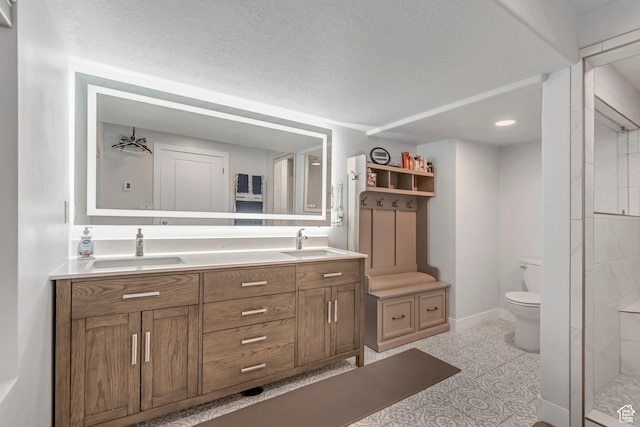 bathroom featuring double vanity, a tile shower, toilet, and a sink