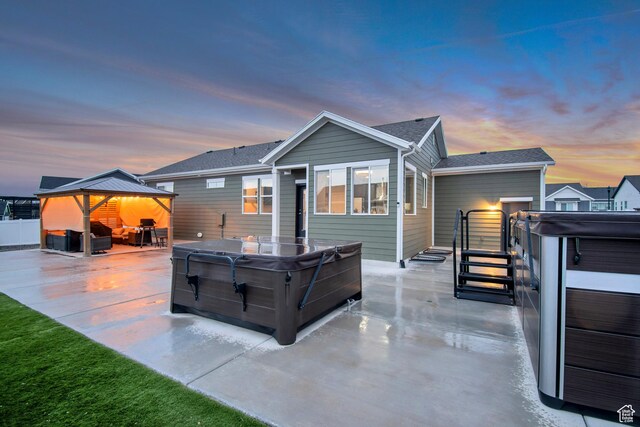 back of house at dusk with fence, a gazebo, a patio area, and a hot tub
