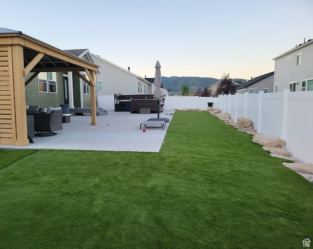 yard at dusk featuring an outdoor hangout area, a fenced backyard, a gazebo, a hot tub, and a patio area