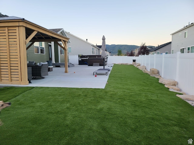 yard at dusk featuring a hot tub, a gazebo, a patio, and a fenced backyard