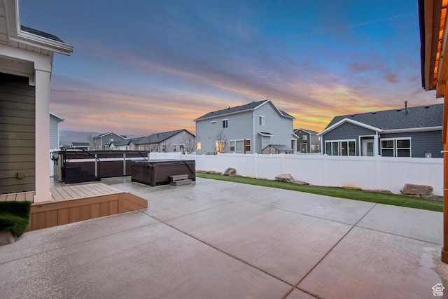 patio terrace at dusk featuring a residential view, fence private yard, and a hot tub