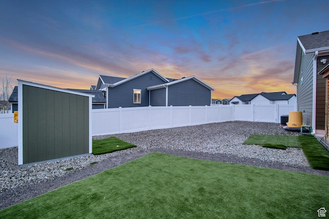 yard at dusk featuring a fenced backyard, a storage unit, cooling unit, and an outbuilding