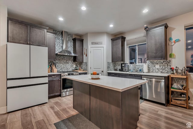 kitchen with light countertops, stainless steel appliances, light wood-style flooring, and wall chimney exhaust hood