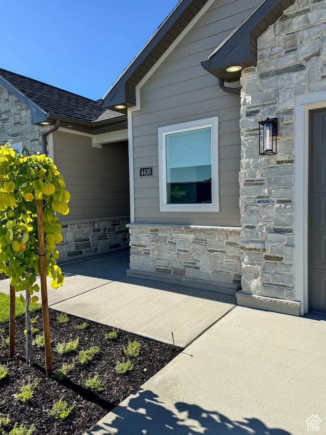 view of exterior entry with stone siding and roof with shingles