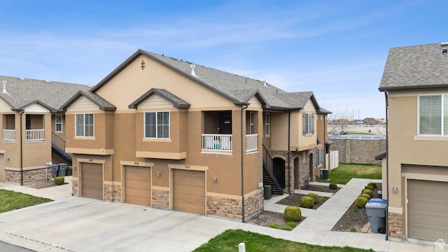 view of property with stucco siding, fence, an attached garage, stone siding, and driveway