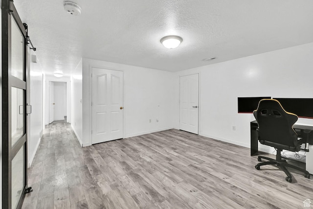 office space featuring baseboards, a textured ceiling, a barn door, visible vents, and light wood finished floors