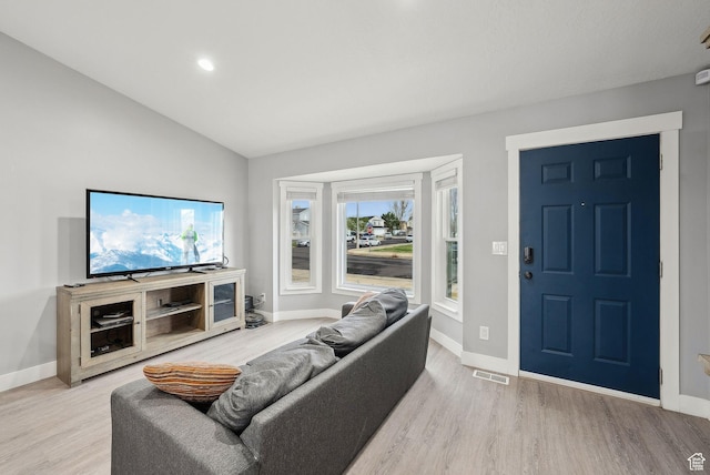 living area featuring baseboards, visible vents, lofted ceiling, and light wood-type flooring