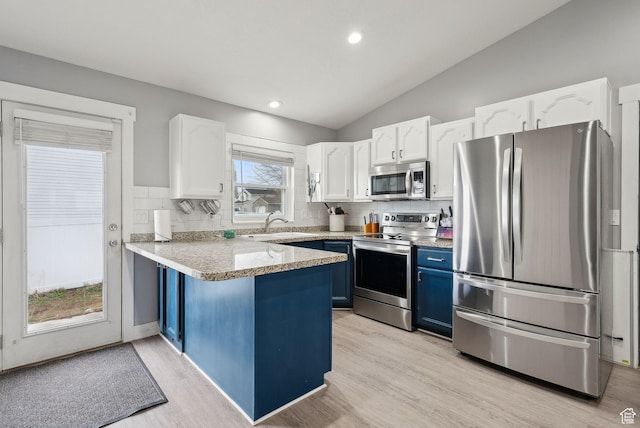 kitchen with blue cabinets, appliances with stainless steel finishes, a peninsula, lofted ceiling, and white cabinets