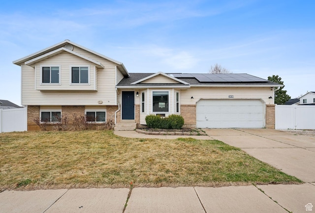 tri-level home with fence, a front yard, brick siding, a garage, and roof mounted solar panels
