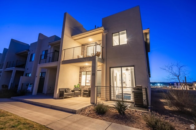 5399 S Cerulean Ln Unit 95, St George, UT 84790 - back of house at night featuring an outdoor hangout area, stucco siding, a patio, stone siding, and a balcony