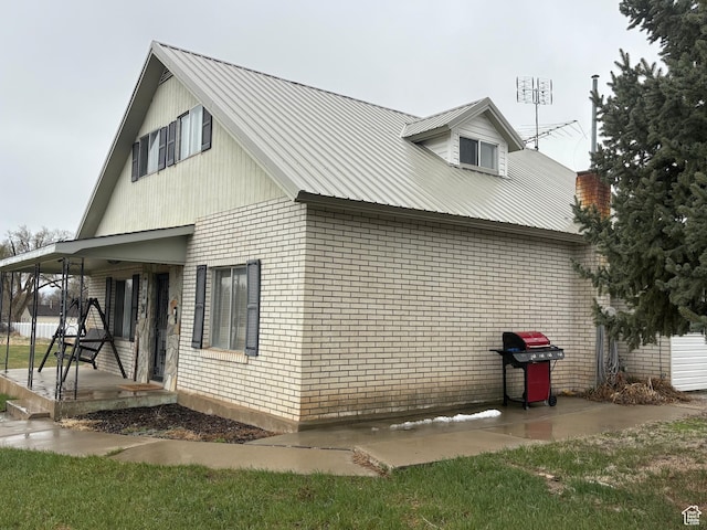 view of side of property featuring covered porch, brick siding, and metal roof