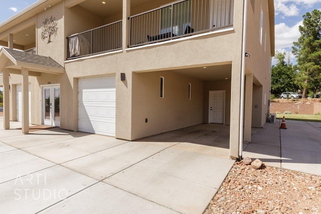 back of house featuring french doors, concrete driveway, stucco siding, an attached garage, and a balcony