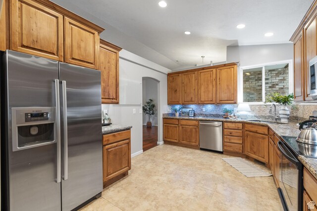 13968 S Hawberry Rd E, Draper, UT 84020 - kitchen with brown cabinetry, stainless steel appliances, arched walkways, stone counters, and backsplash