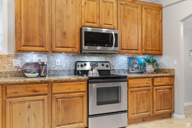 13968 S Hawberry Rd E, Draper, UT 84020 - kitchen featuring backsplash, baseboards, stainless steel appliances, light stone counters, and brown cabinetry