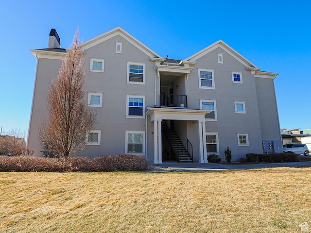back of property with a lawn, a chimney, stucco siding, and stairway