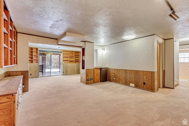 basement with a textured ceiling, wallpapered walls, carpet floors, and wainscoting