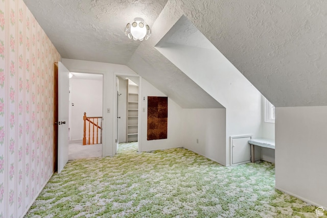 bonus room with lofted ceiling, a textured ceiling, wallpapered walls, and carpet
