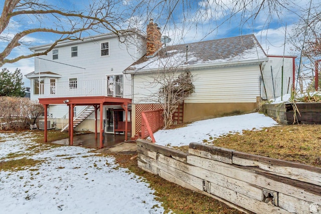 snow covered property featuring a wooden deck, stairway, roof with shingles, and a chimney