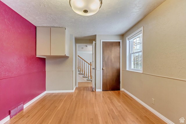 unfurnished room with light wood-style flooring, a textured ceiling, stairs, and visible vents