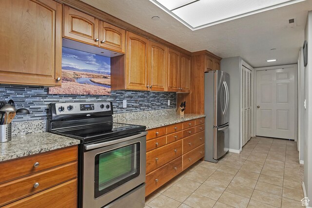 3125 E Kennedy Dr S Unit 605, Salt Lake City, UT 84108 - kitchen featuring light tile patterned floors, stainless steel appliances, light stone counters, and brown cabinets