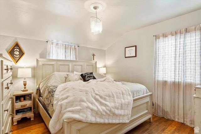 bedroom with a chandelier, vaulted ceiling, and wood finished floors