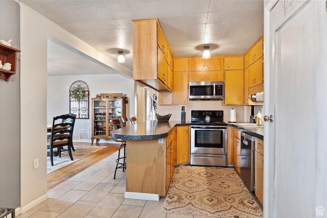 kitchen featuring appliances with stainless steel finishes, a peninsula, dark countertops, baseboards, and visible vents