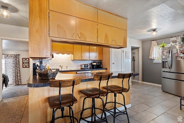 kitchen with a breakfast bar area, dark countertops, stainless steel refrigerator with ice dispenser, and decorative backsplash